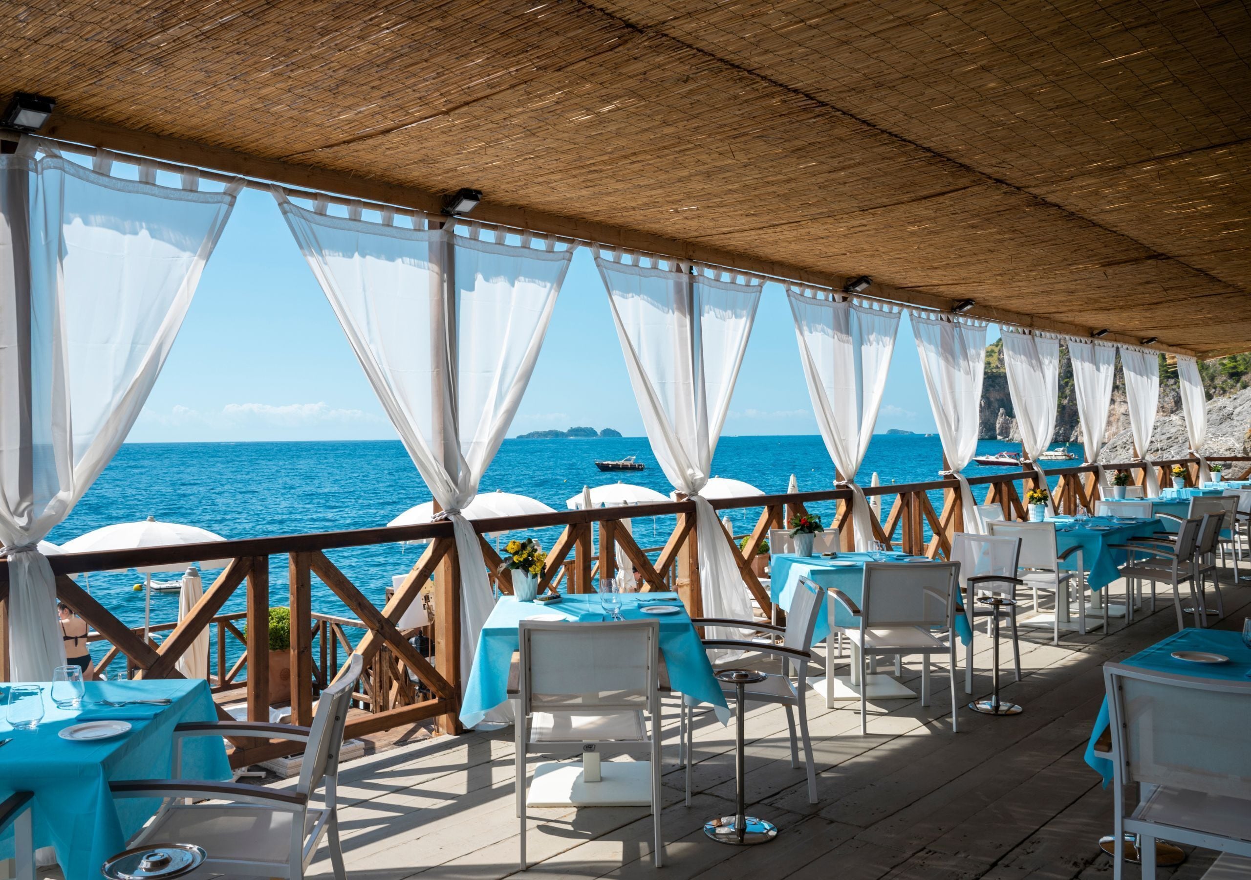 Un área de comedor al aire libre con mesas y sillas, con vista al mar.