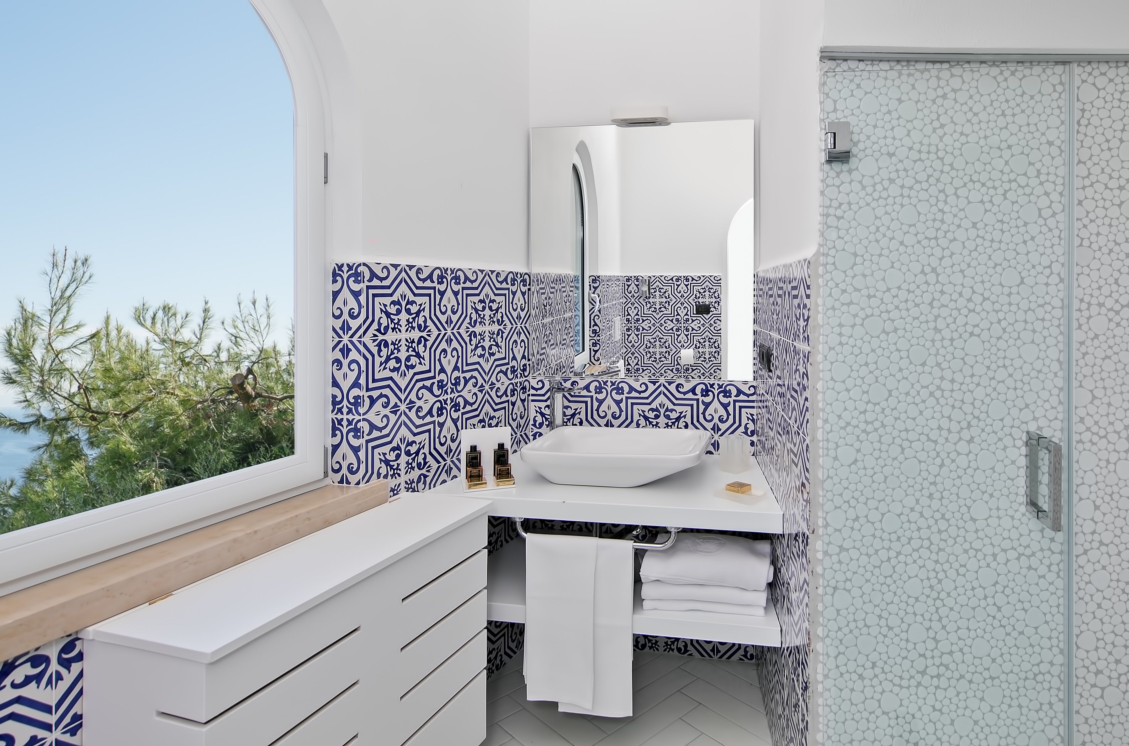 A modern bathroom with a white sink, a mirror, and patterned tiles.