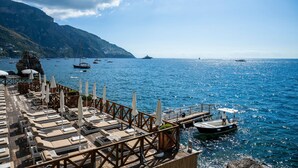 A seaside restaurant with outdoor seating, a dock, and boats in the background. - Hotel Le Agavi (Positano)