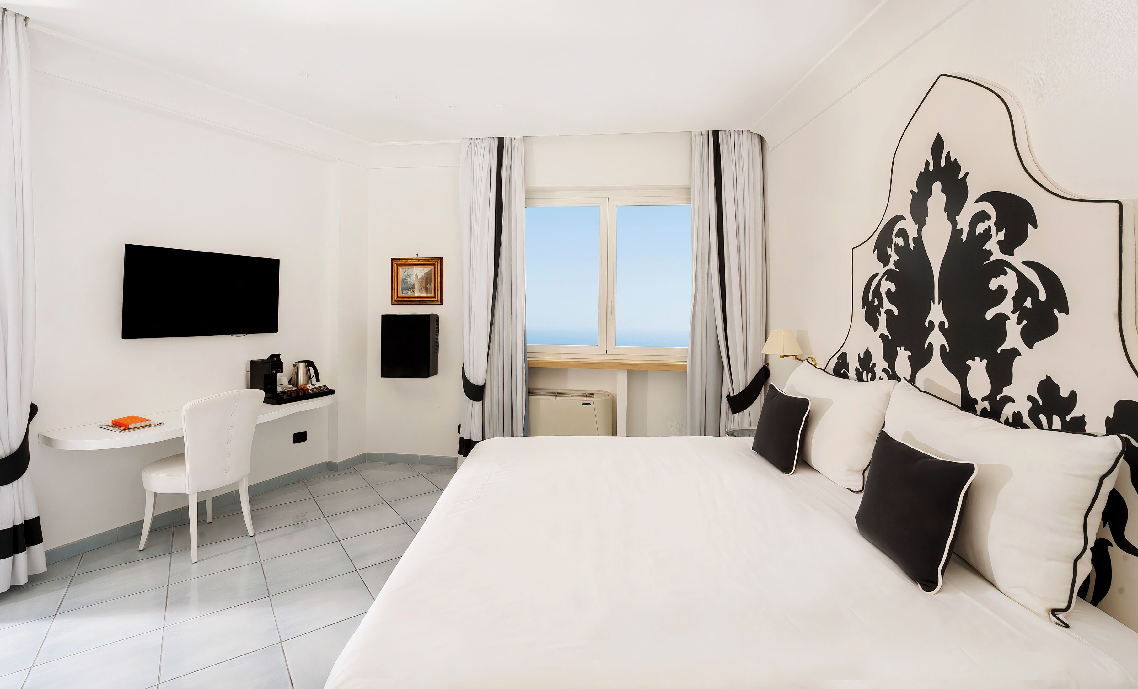 A hotel room with a large bed, a desk with a chair, a TV, and a window with curtains.