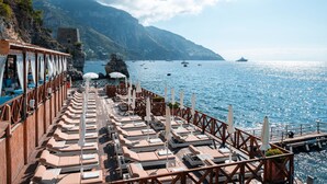 A sun deck with lounge chairs and umbrellas overlooking a coastal sea. - Hotel Le Agavi (Positano)