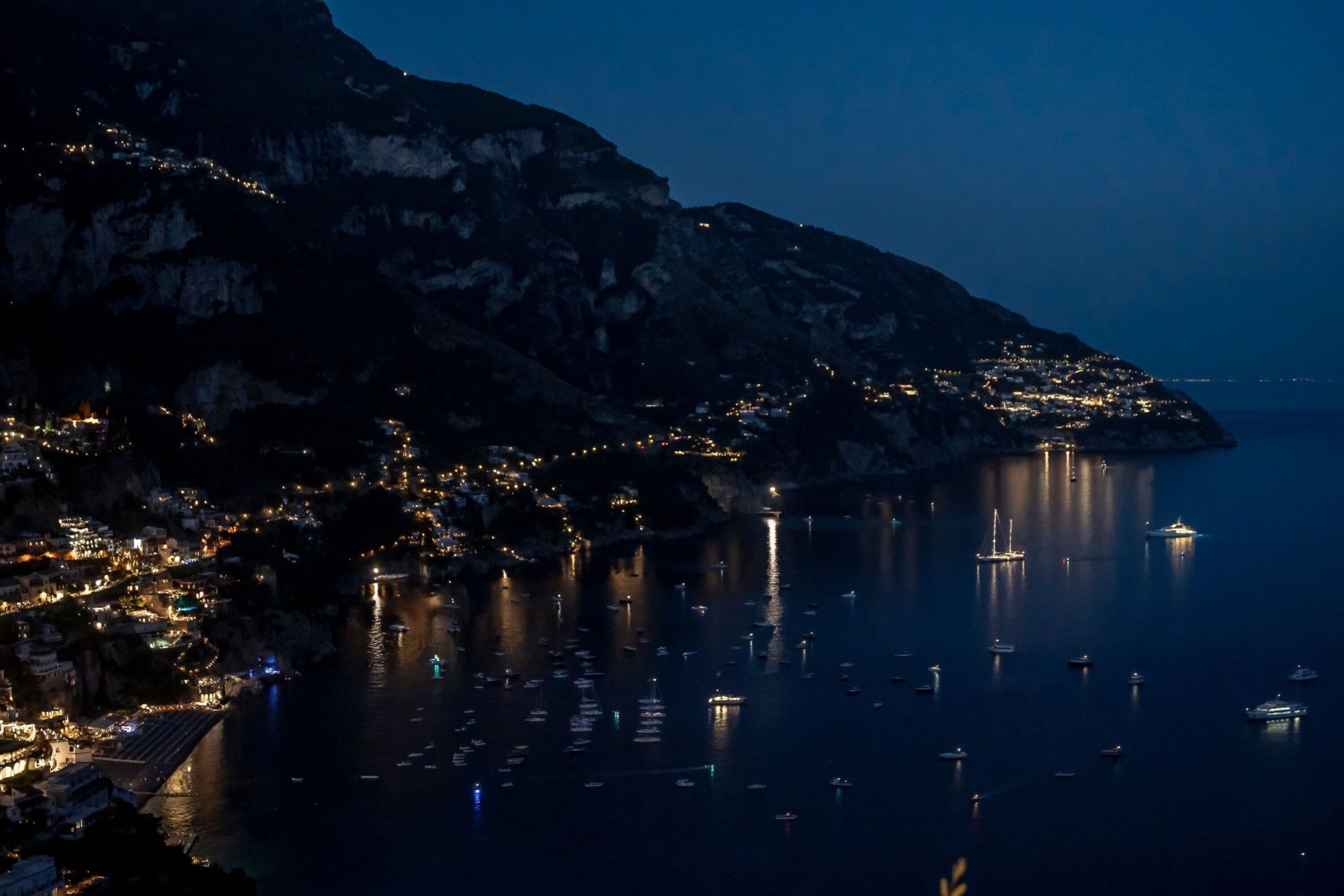 A coastal town at night with illuminated buildings and boats on the water.