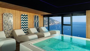 A modern indoor pool area with a view of the sea, wooden paneling, and patterned cushions. - Hotel Le Agavi (Positano)