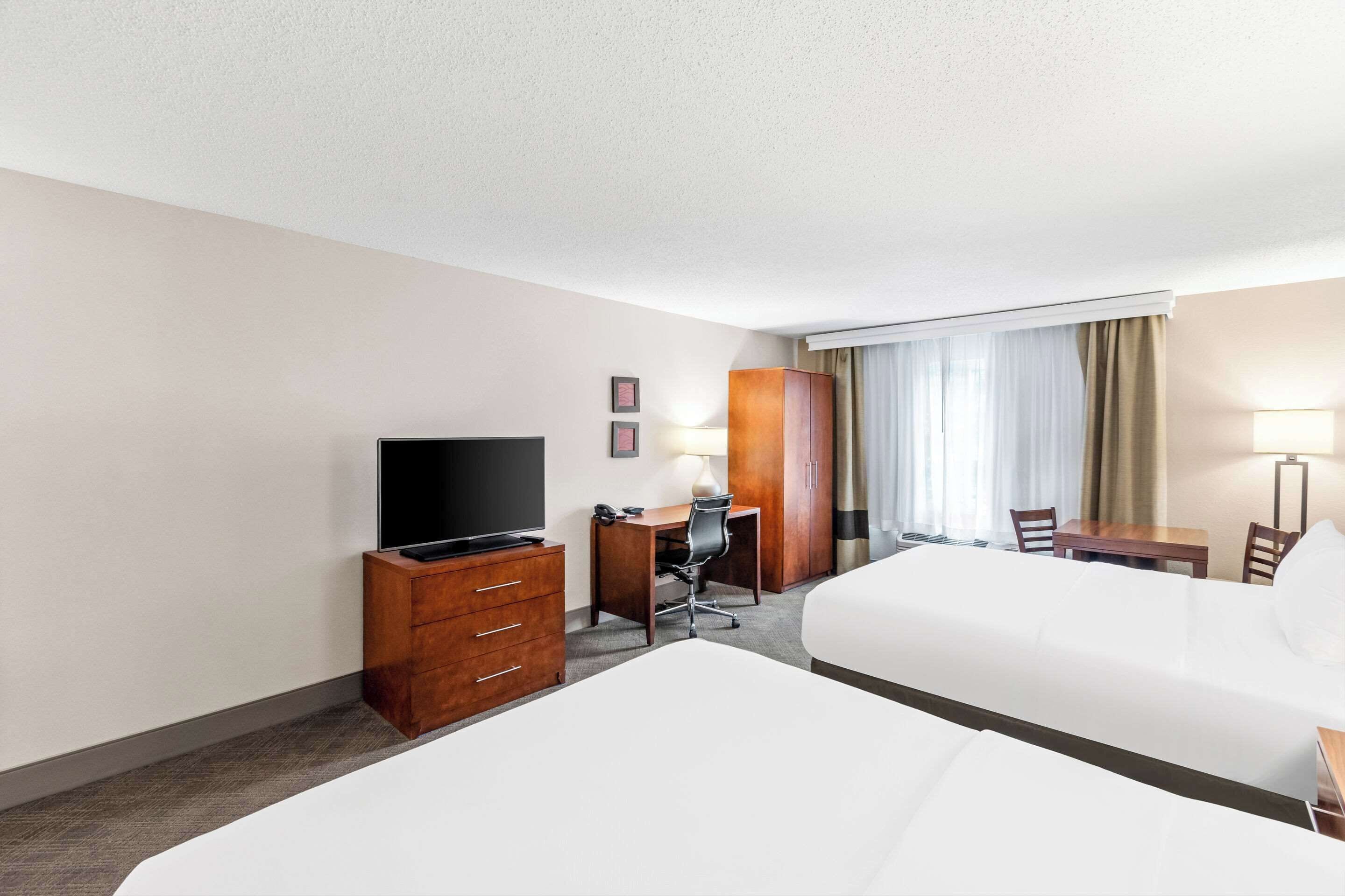 Ein Hotelzimmer mit zwei Betten, einem Schreibtisch mit Stuhl, einem Fernseher, einem Kleiderschrank und einem Fenster mit Vorhängen.