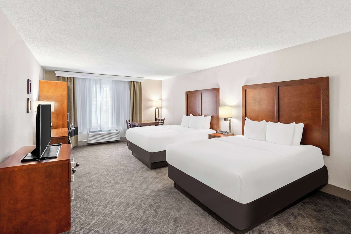 A hotel room with two beds, a desk, a TV, and a window with curtains.