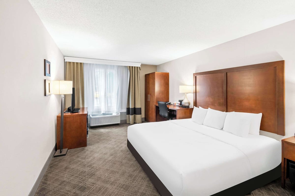 A hotel room with a large bed, a desk, a chair, a lamp, and a wardrobe.
