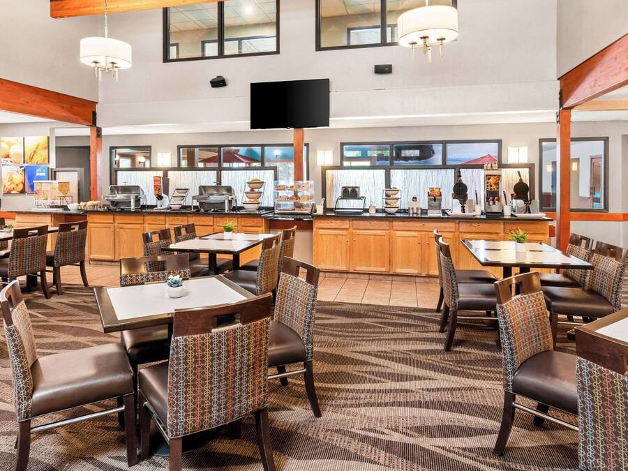 Ein Hotel-Speisesaal mit mehreren Tischen und Stühlen, einer zentralen Theke mit Speisenauslagen und einem an der Wand befestigten Fernseher.
