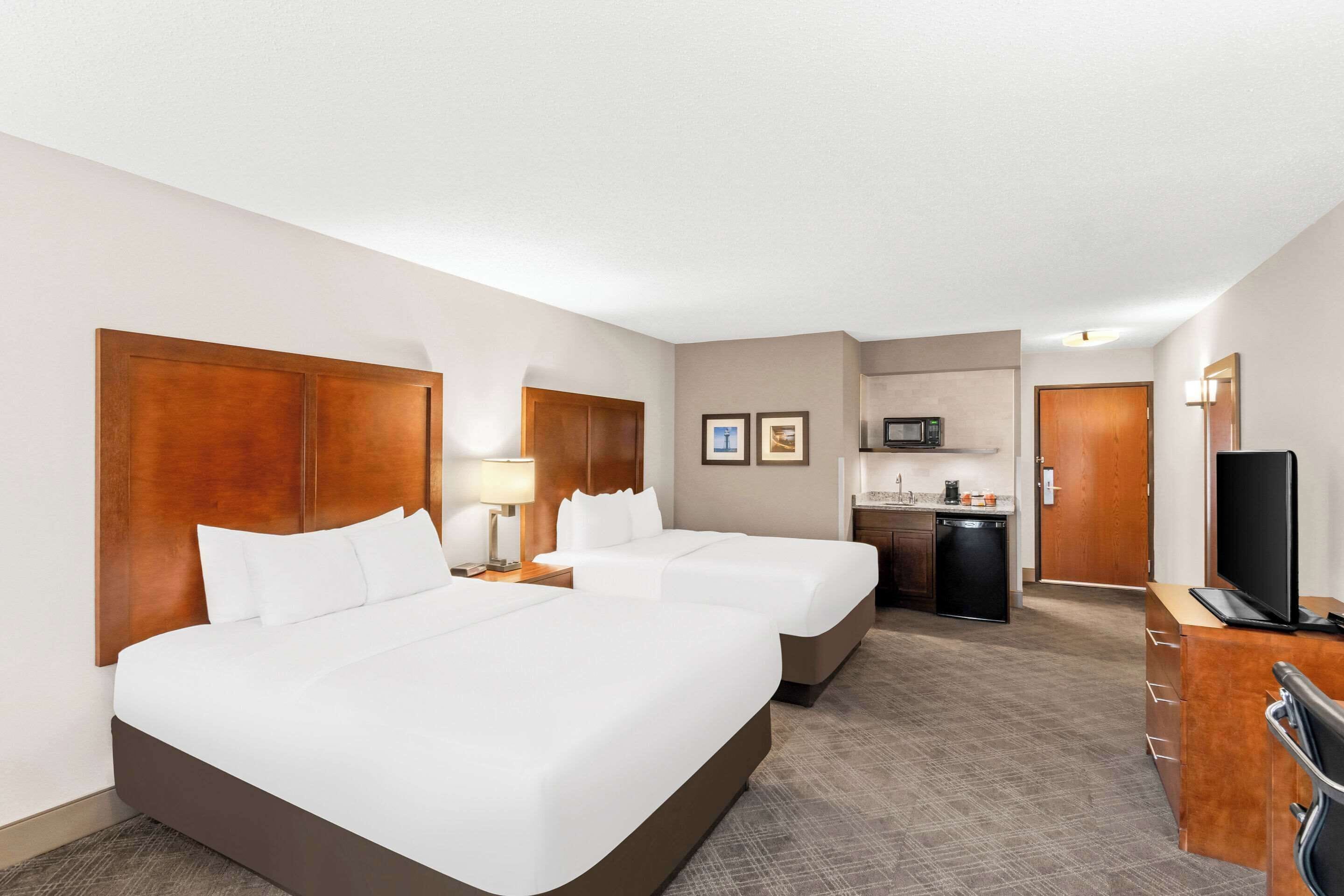 A hotel room with two beds, a desk, a microwave, and a television.