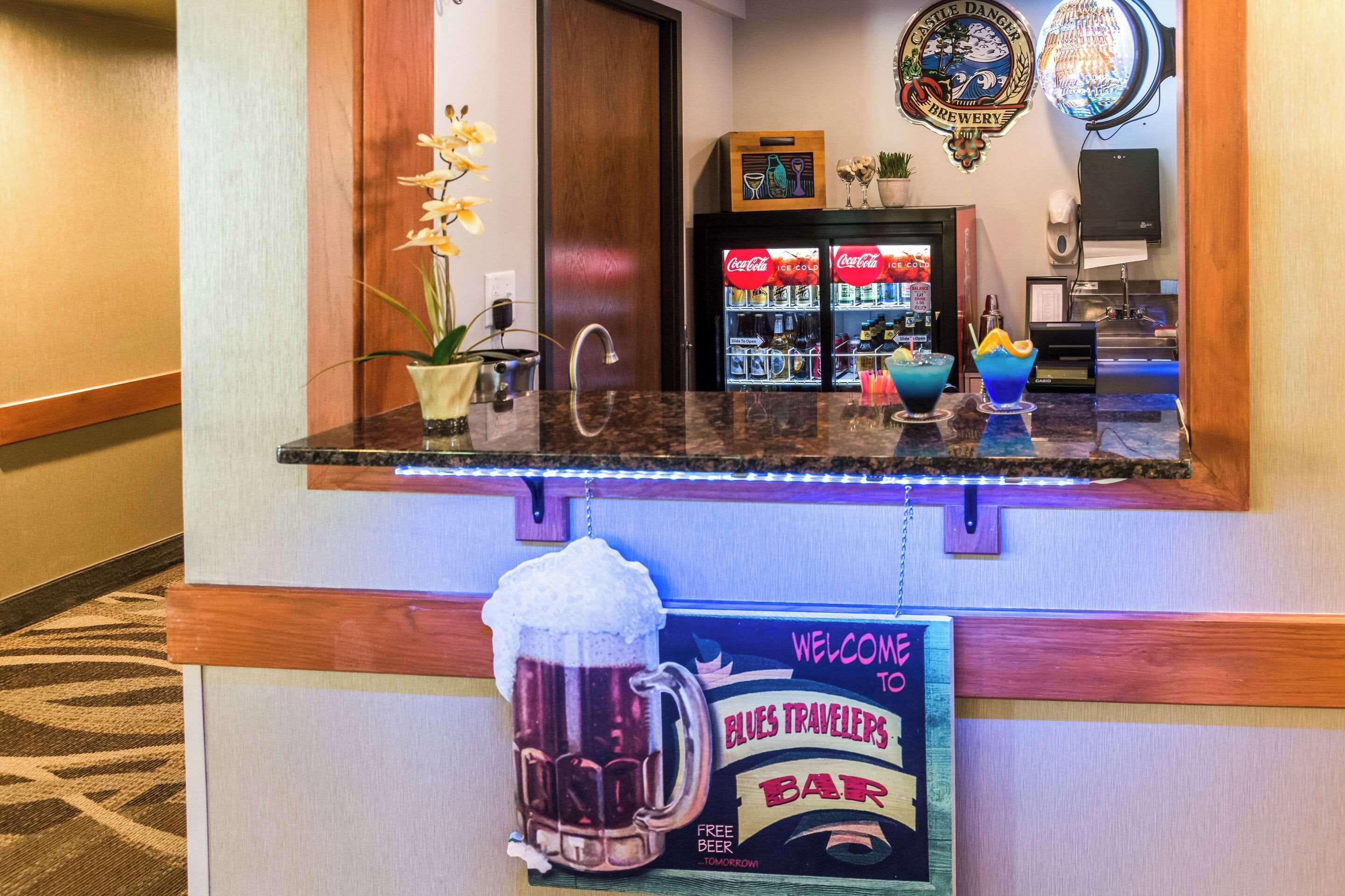 A bar area with a Coca-Cola refrigerator, a sign for 'Elvis Travelers Bar', and a large beer mug.