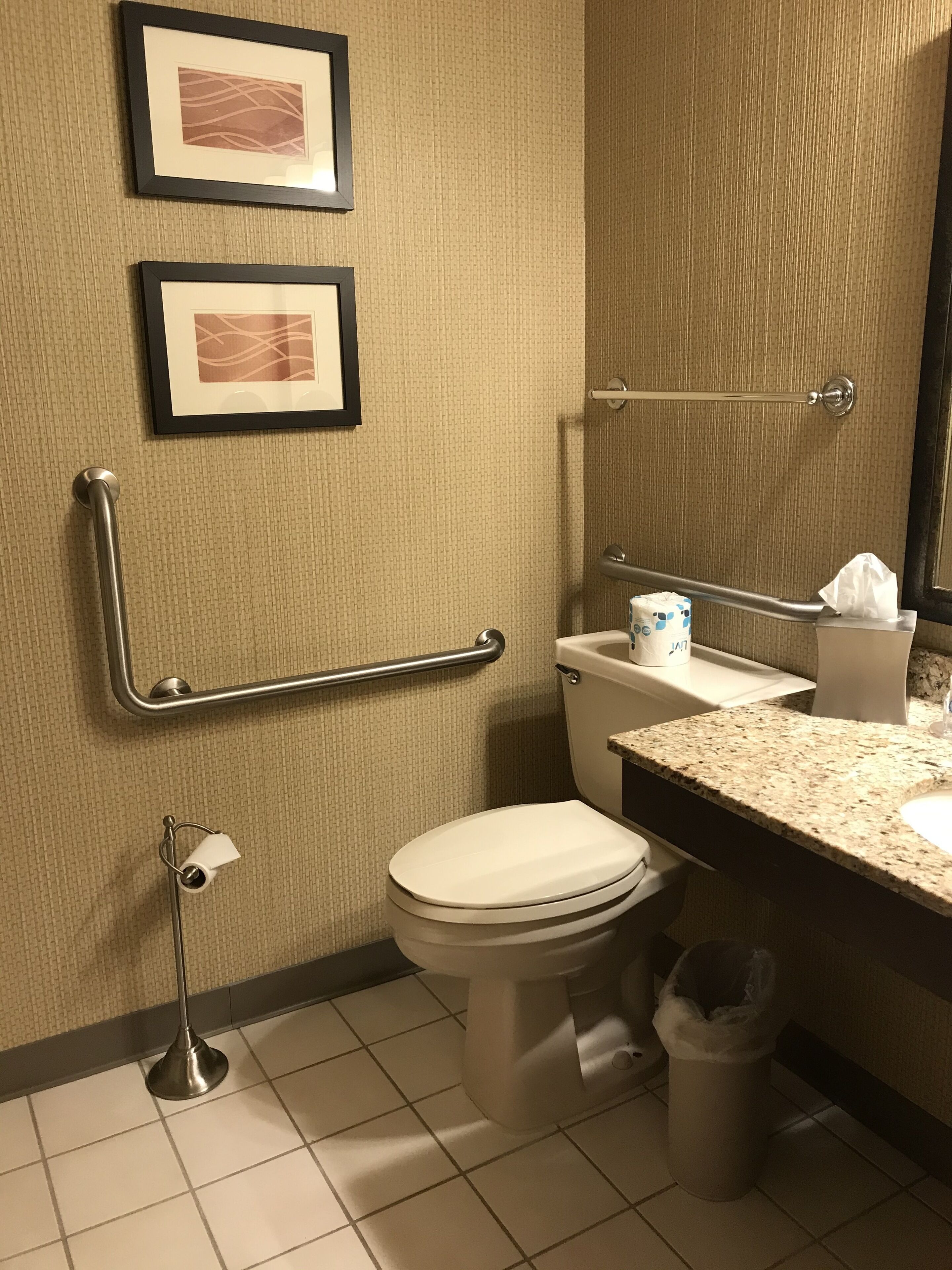 Een badkamer met toilet, bidet, wastafel en afbeeldingen in lijsten aan de muur.