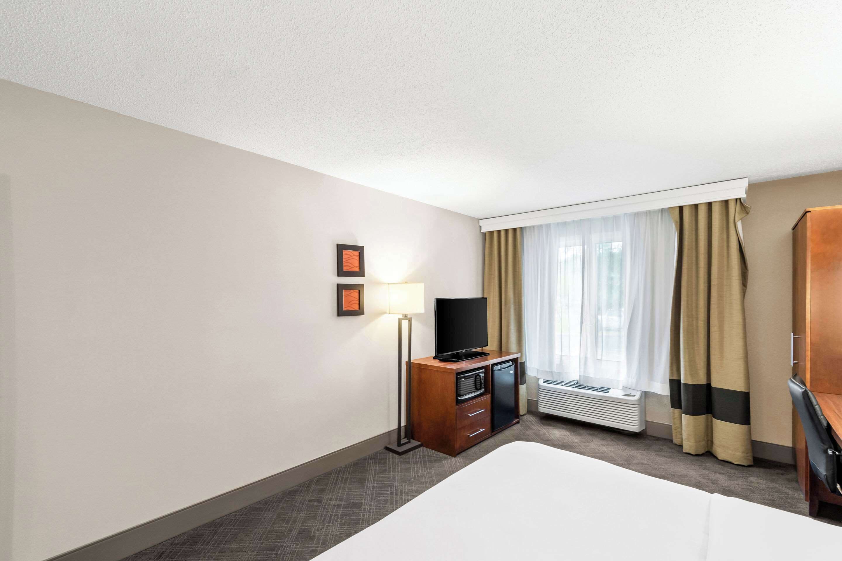 Una habitación de hotel con una cama, un televisor sobre un mueble de madera, un escritorio y una ventana con cortinas.