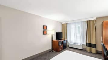 Una habitación de hotel con una cama, un televisor sobre un mueble de madera, un escritorio y una ventana con cortinas.