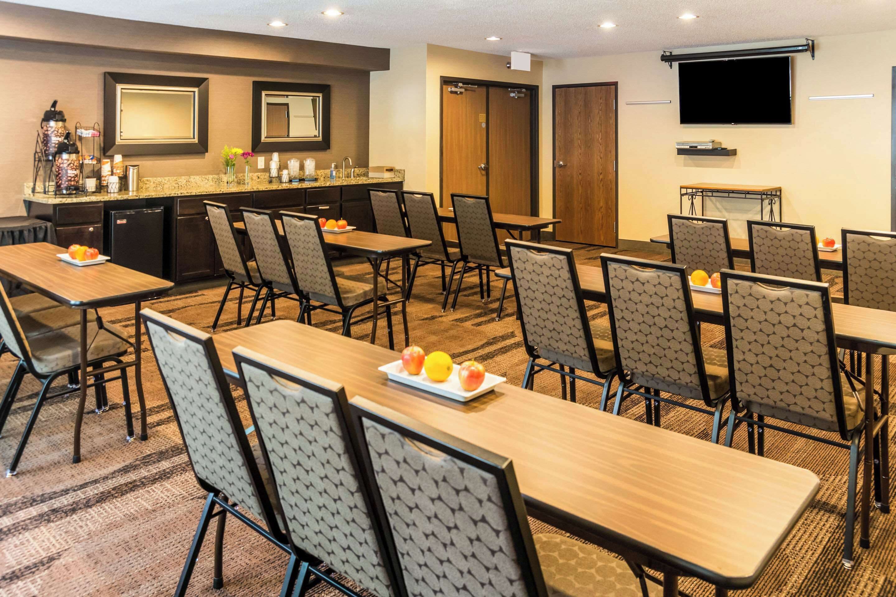 Uma sala de conferências de hotel com várias mesas e cadeiras, uma copa, uma televisão e uma porta.