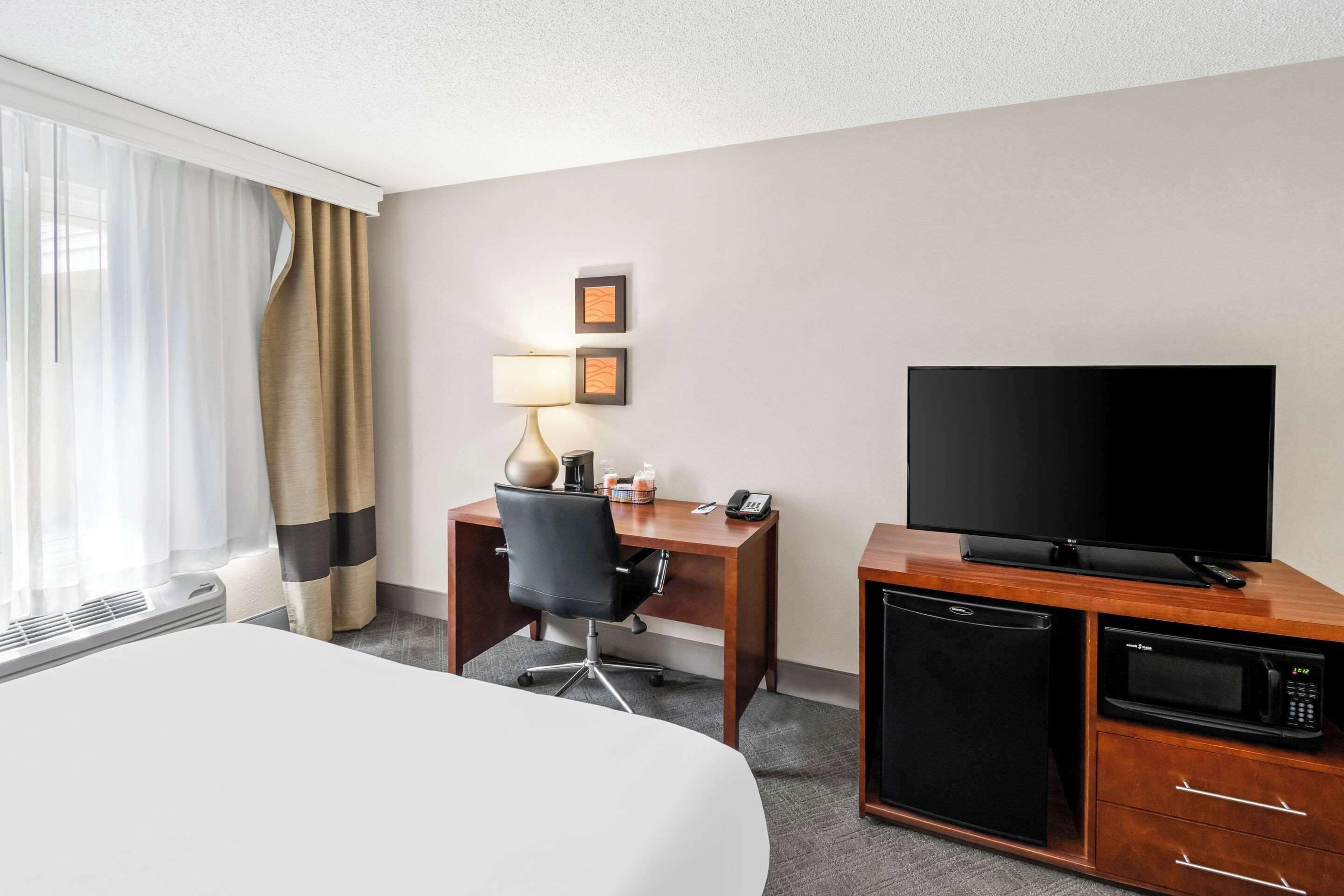 Une chambre d’hôtel équipée d’un lit, d’un bureau avec une chaise, d’une télévision, d’un four à micro-ondes et d’un mini-réfrigérateur.