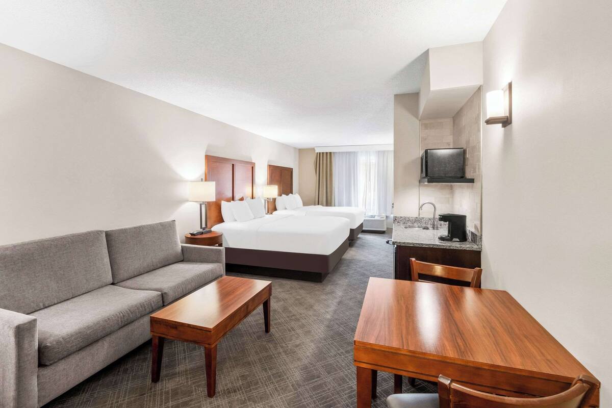 A hotel room with a bed, a sofa, a dining table, a TV, and a kitchenette.