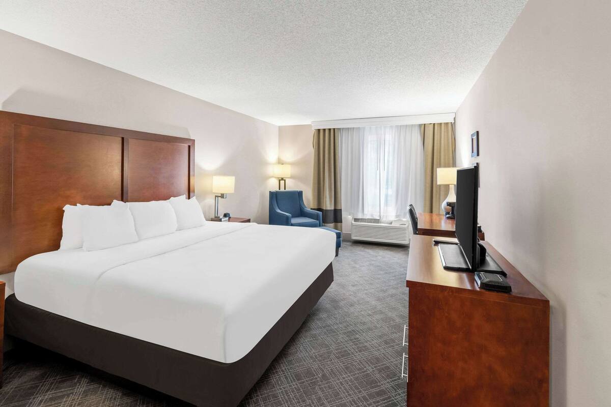 A hotel room with a large bed, a desk with a computer, a chair, and a TV.