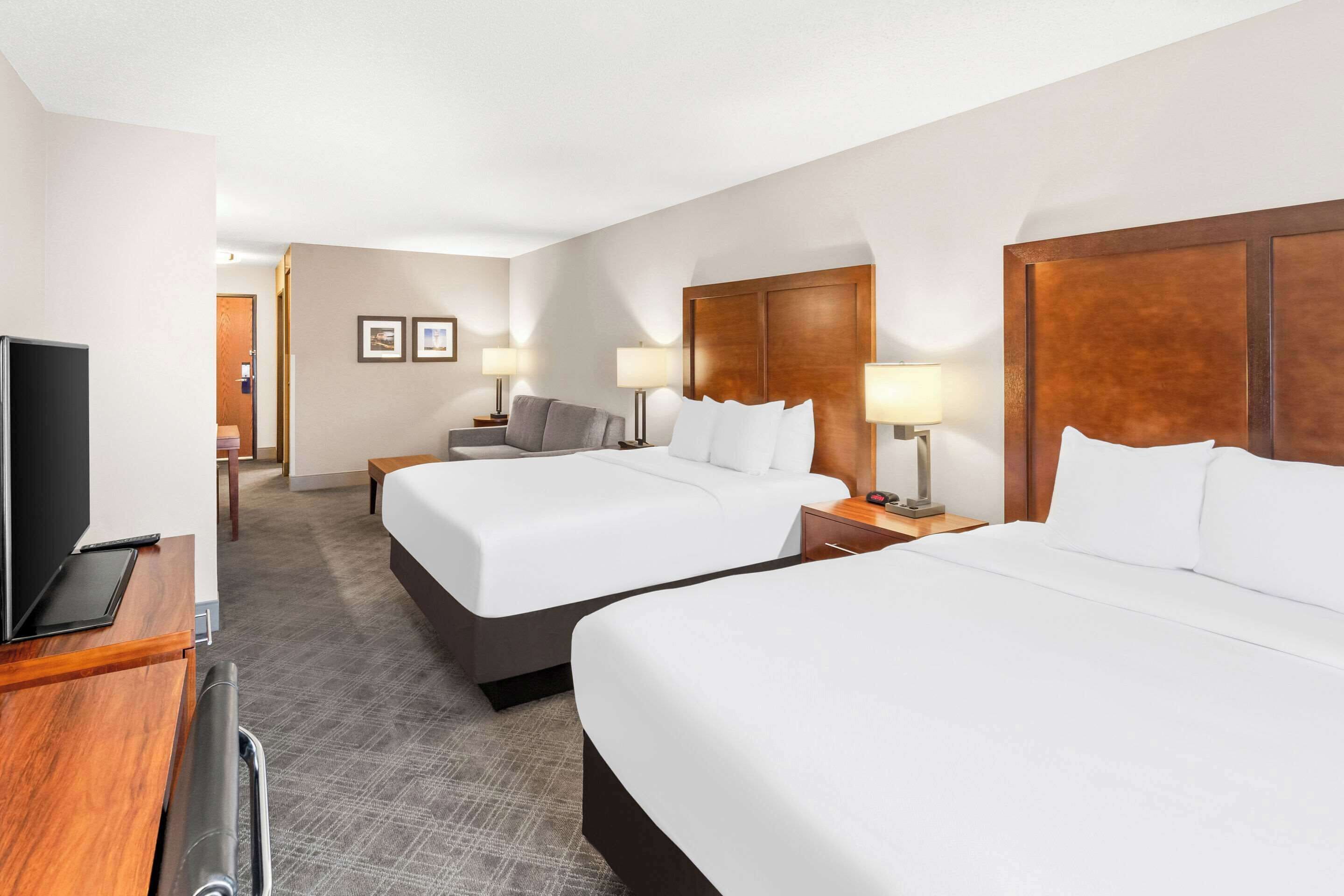Una habitación de hotel con dos camas, un escritorio con televisor y una pequeña zona de estar con sofá y lámparas.