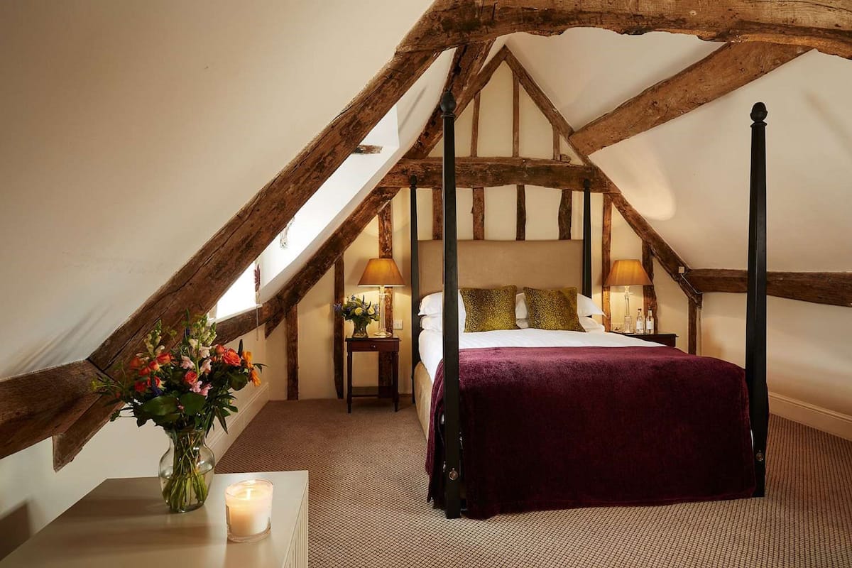 A bedroom with a four-poster bed, a vase with flowers, two bedside lamps, and a wooden ceiling structure.