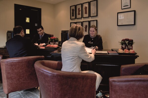 A reception area with leather chairs, a reception desk, framed artwork on the wall, and a door in the background. - Macdonald Bear Hotel (Woodstock)