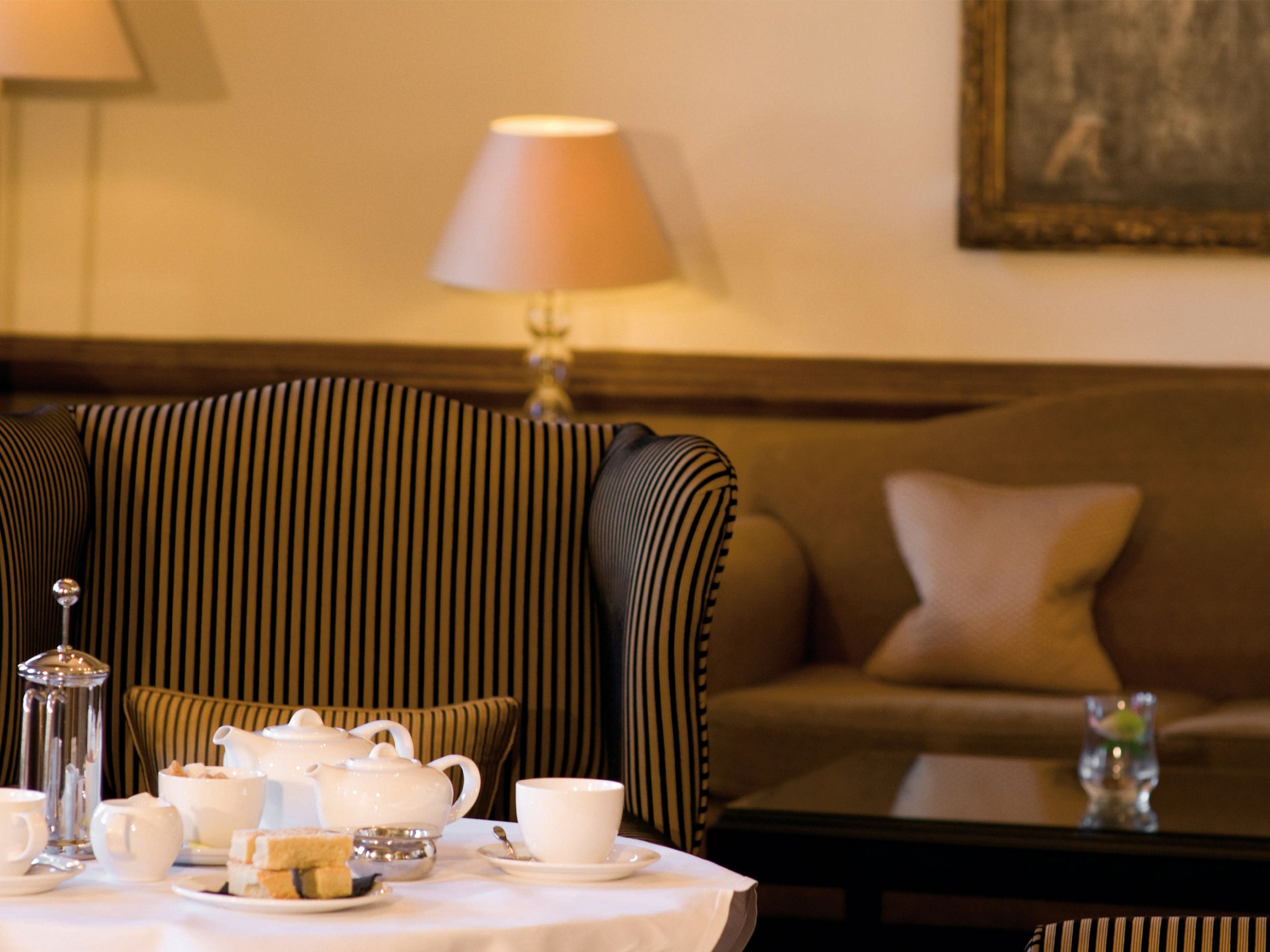 A dining area with a table set for tea, a striped armchair, and a sofa.