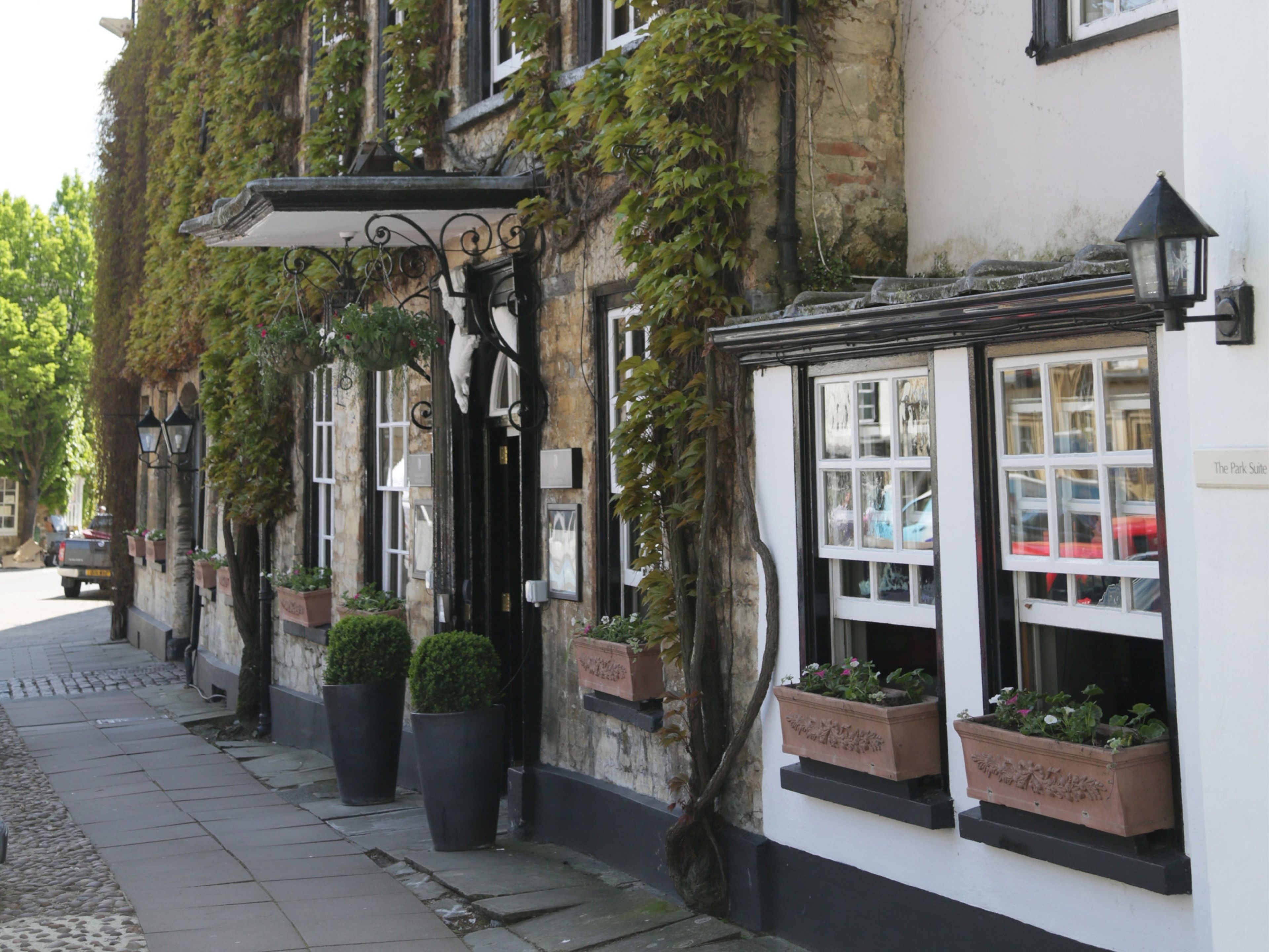 A traditional building with ivy-covered walls, a black awning, and flower boxes on the windows.