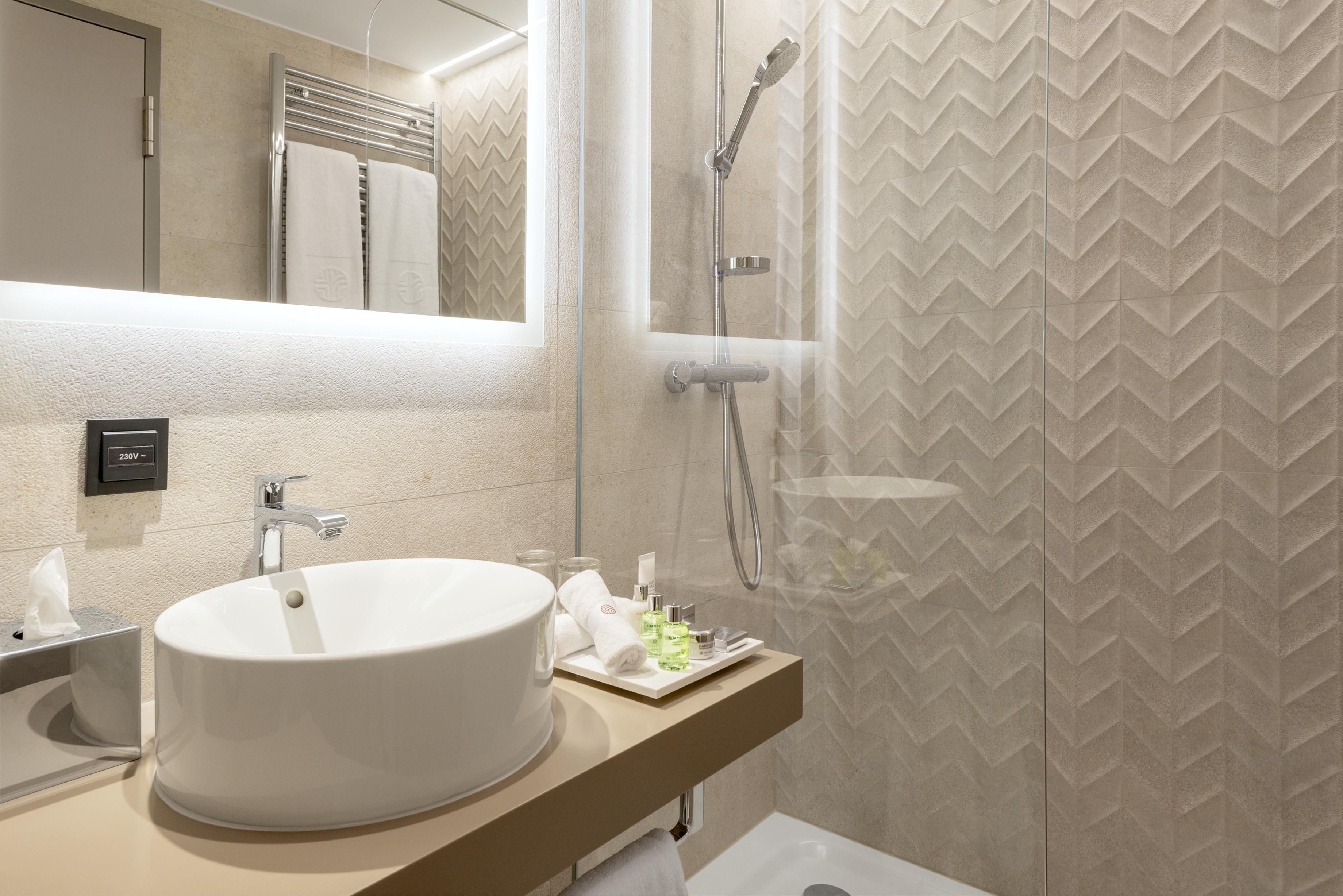 Un baño moderno con un lavamanos grande de color blanco, un cabezal de ducha de mano y un espejo con toallero.