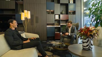 Dos hombres sentados en un sofá en una habitación moderna con estanterías empotradas y una mesa de centro.
