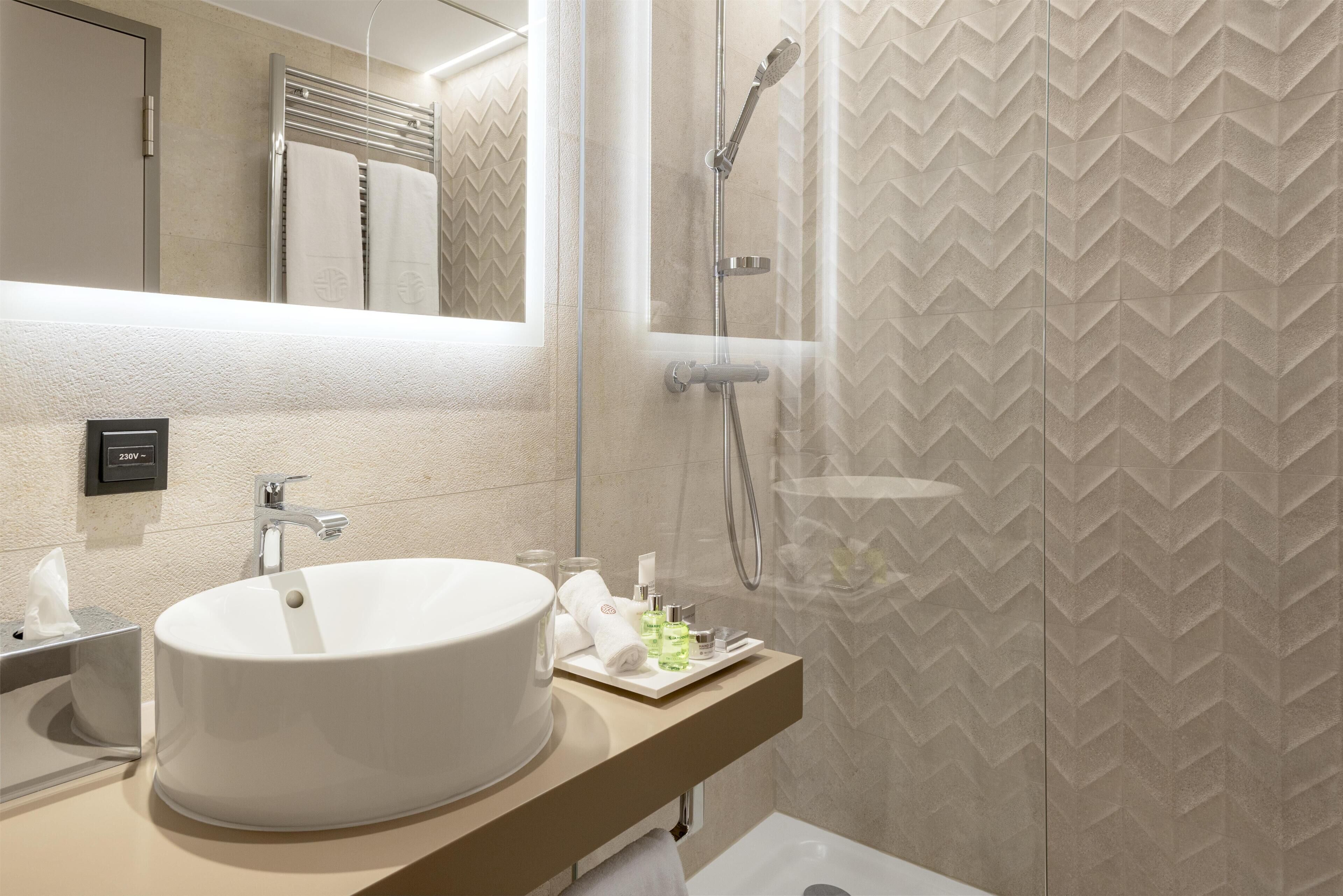 A modern bathroom with a large white sink, a mirror, a towel rack, and a shower area.