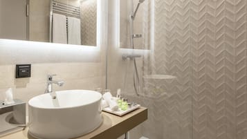 A modern bathroom with a large white sink, a mirror, a towel rack, and a shower area.