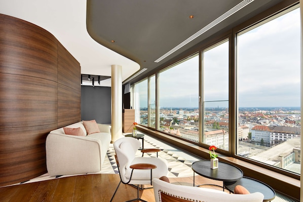 A modern interior with a curved wooden wall, a sofa, chairs, and a view of a cityscape through large windows.