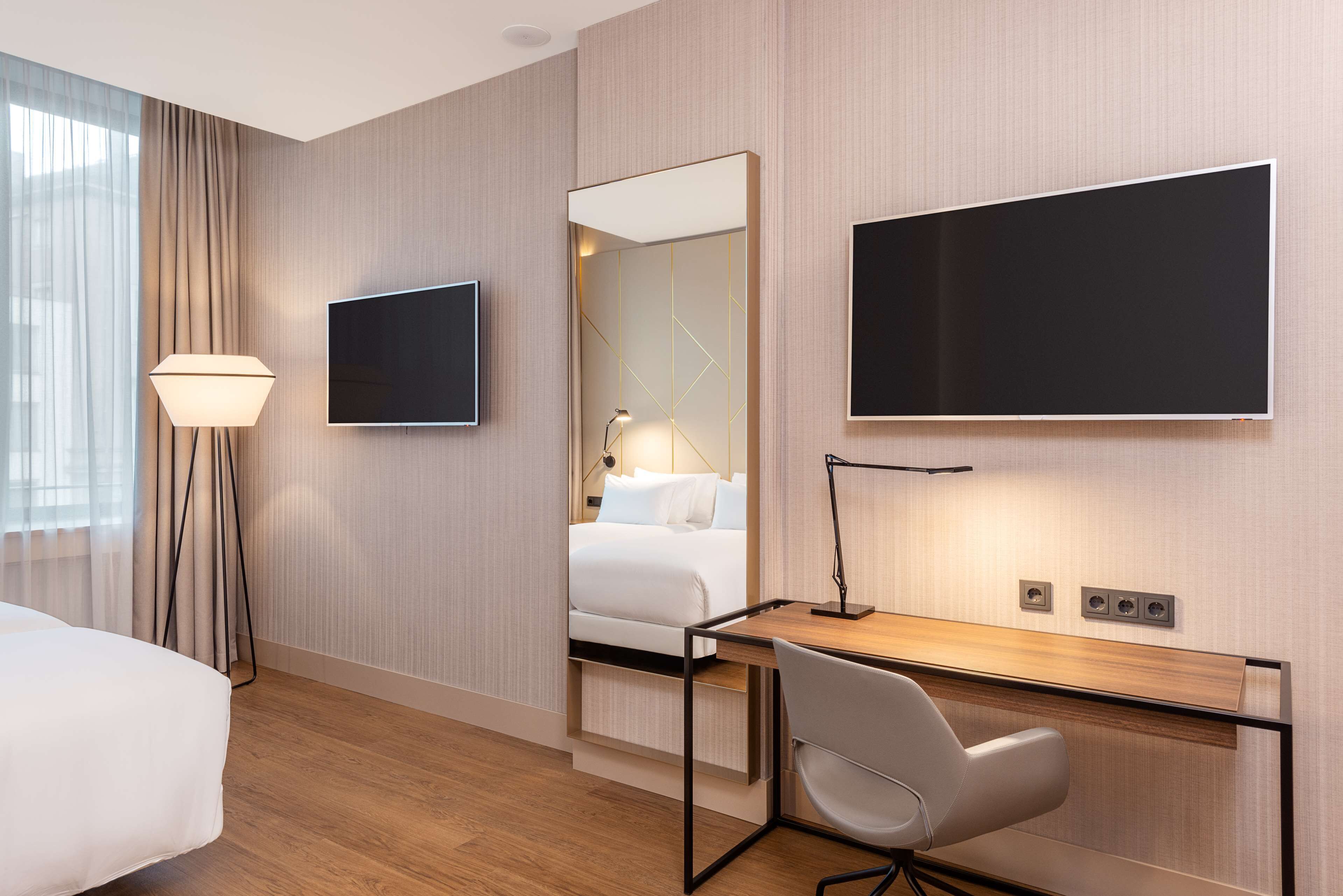 A hotel room with a bed, a desk, a chair, a TV, and a mirror.
