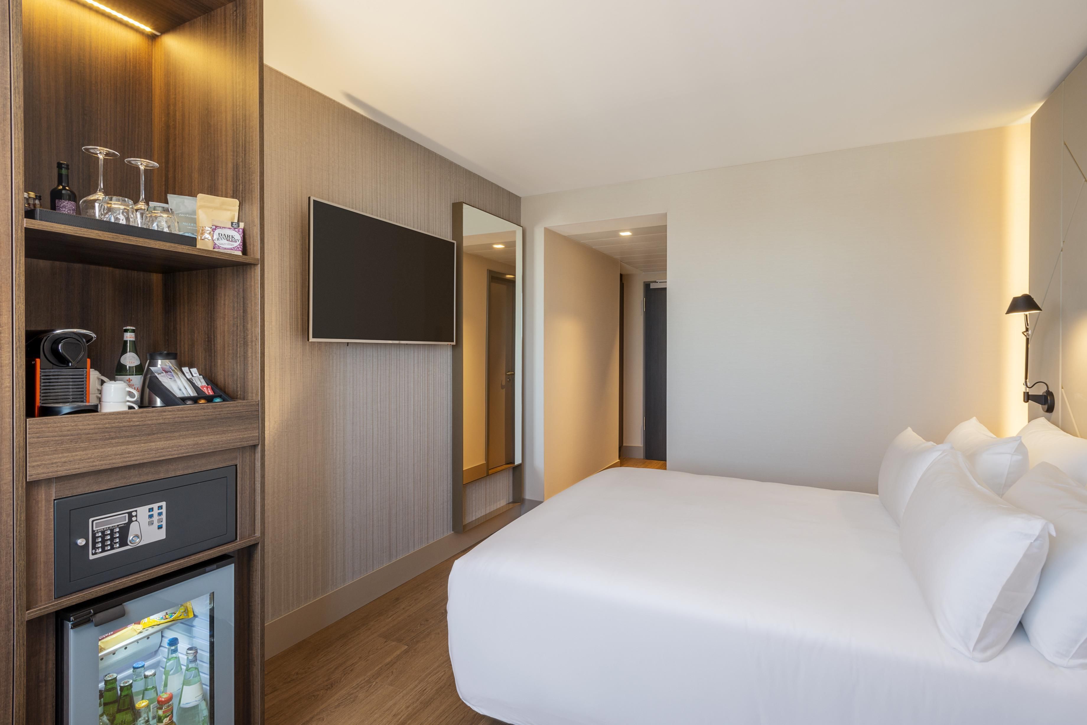 Een hotelkamer met een bed, een aan de muur bevestigde televisie, een minibar en een kleine koelkast.