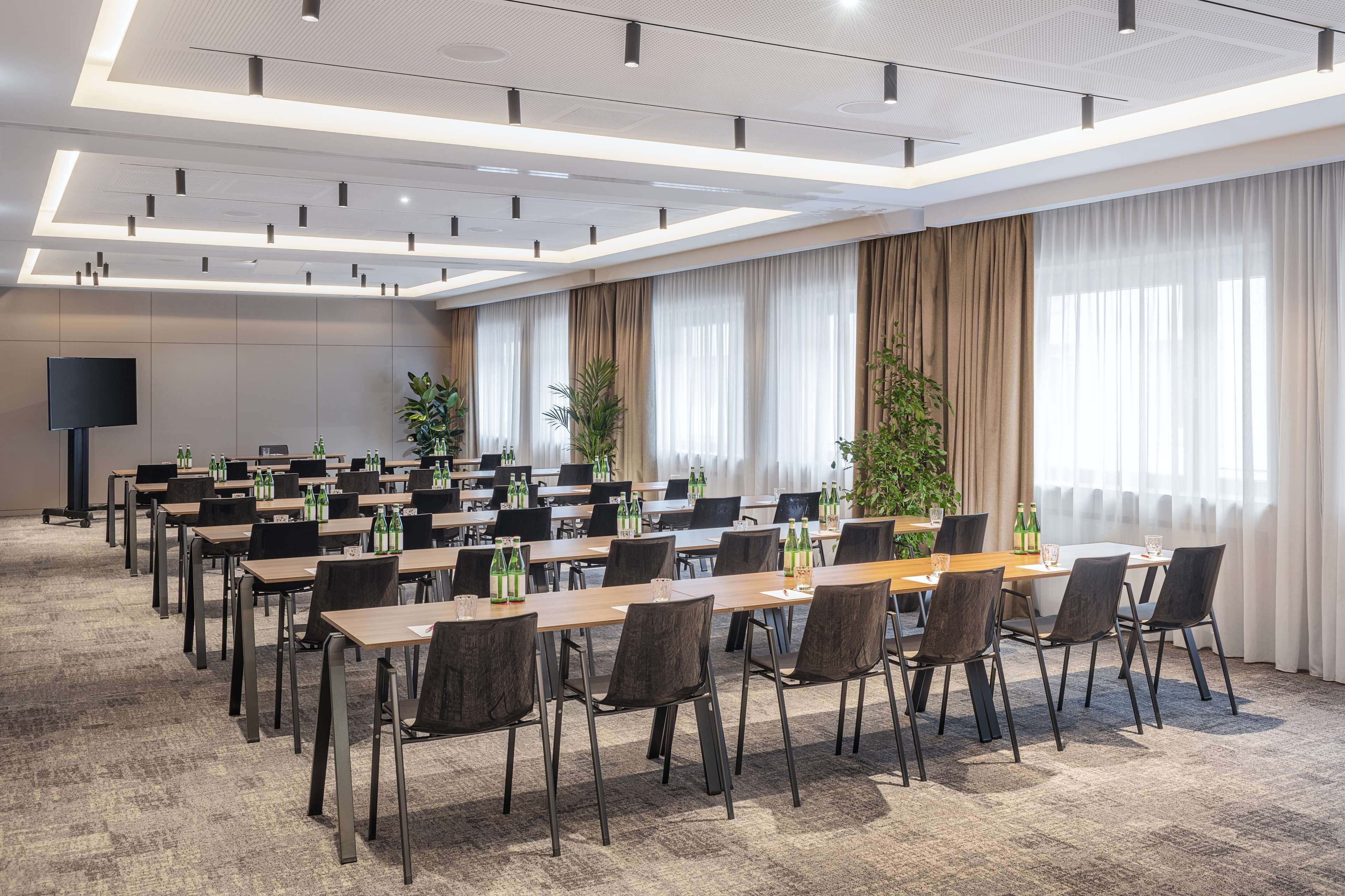 Ein Konferenzraum mit mehreren Tischen und Stühlen, einem großen Flachbildfernseher und großen Fenstern mit Vorhängen.
