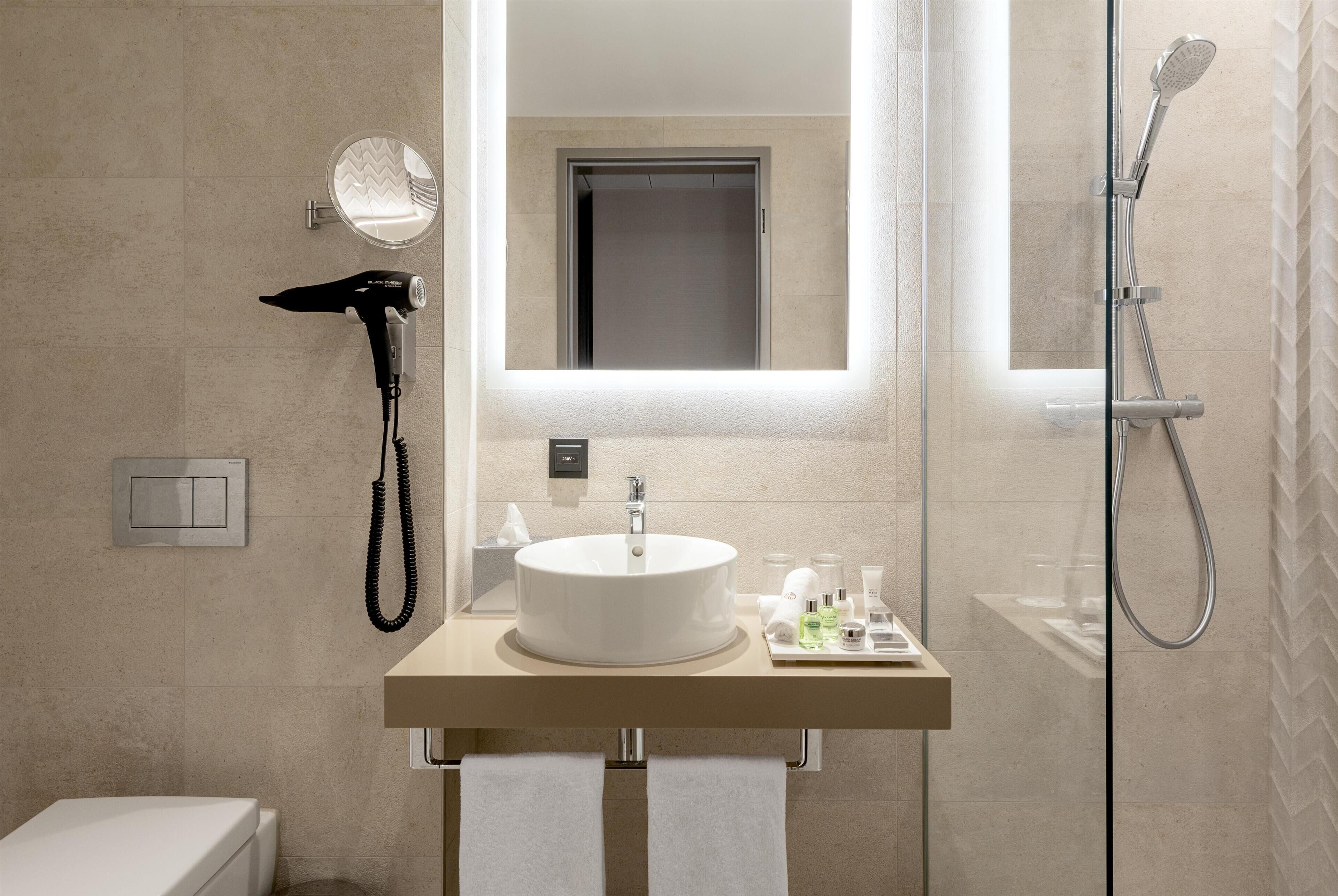 A modern bathroom with a round sink, a hairdryer, a mirror, and a shower.