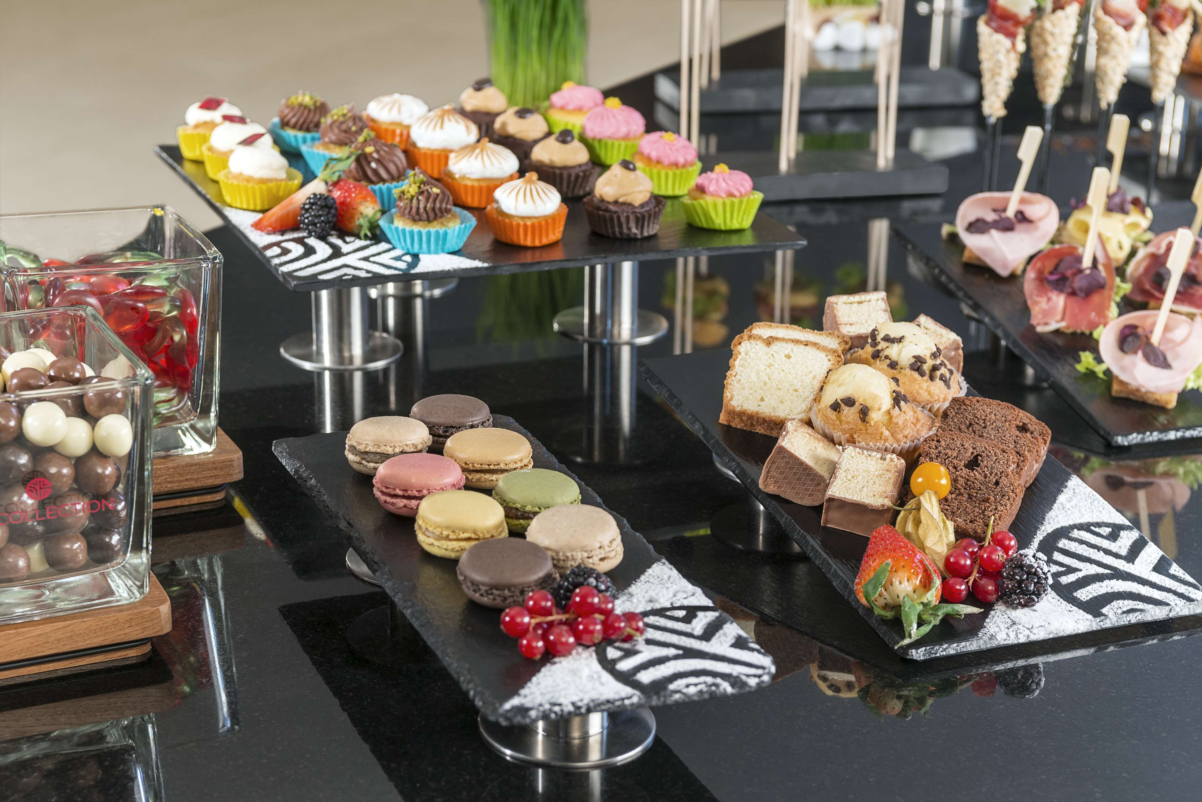 Eine Auswahl an Desserts auf einem Glastisch, darunter Cupcakes, Macarons und Sandwiches.