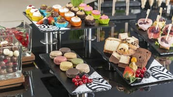 Eine Auswahl an Desserts auf einem Glastisch, darunter Cupcakes, Macarons und Sandwiches.