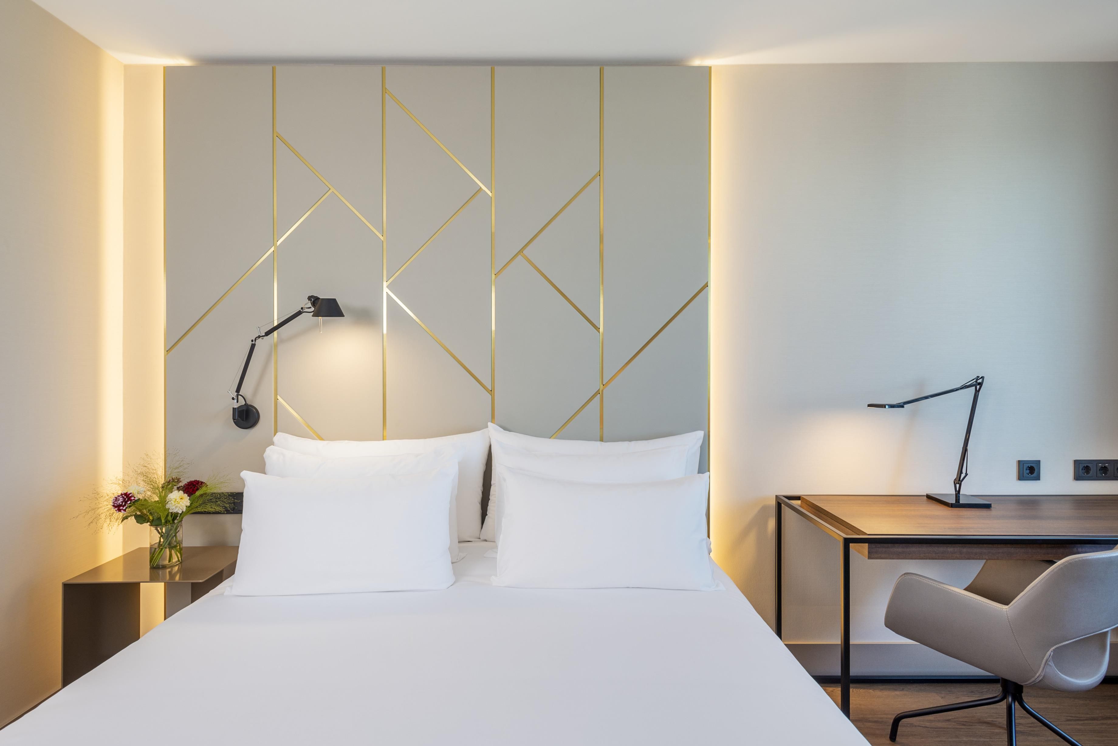 A modern hotel room with a bed, bedside table, desk, and chair.