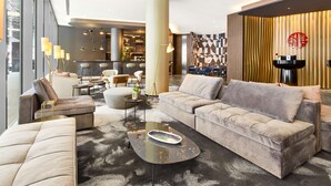 Una sala moderna con sofá, sillones y una mesa de centro. Se observa una cocina al fondo con taburetes de bar.