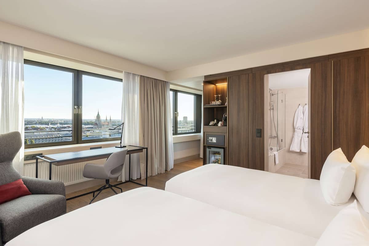 A hotel room with a large bed, a desk, a chair, and a view of the cityscape.