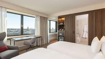 A hotel room with a large bed, a desk, a chair, and a view of the cityscape.