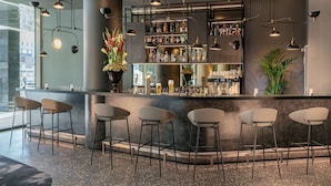 Una zona de bar con mostrador, taburetes y luces colgantes.