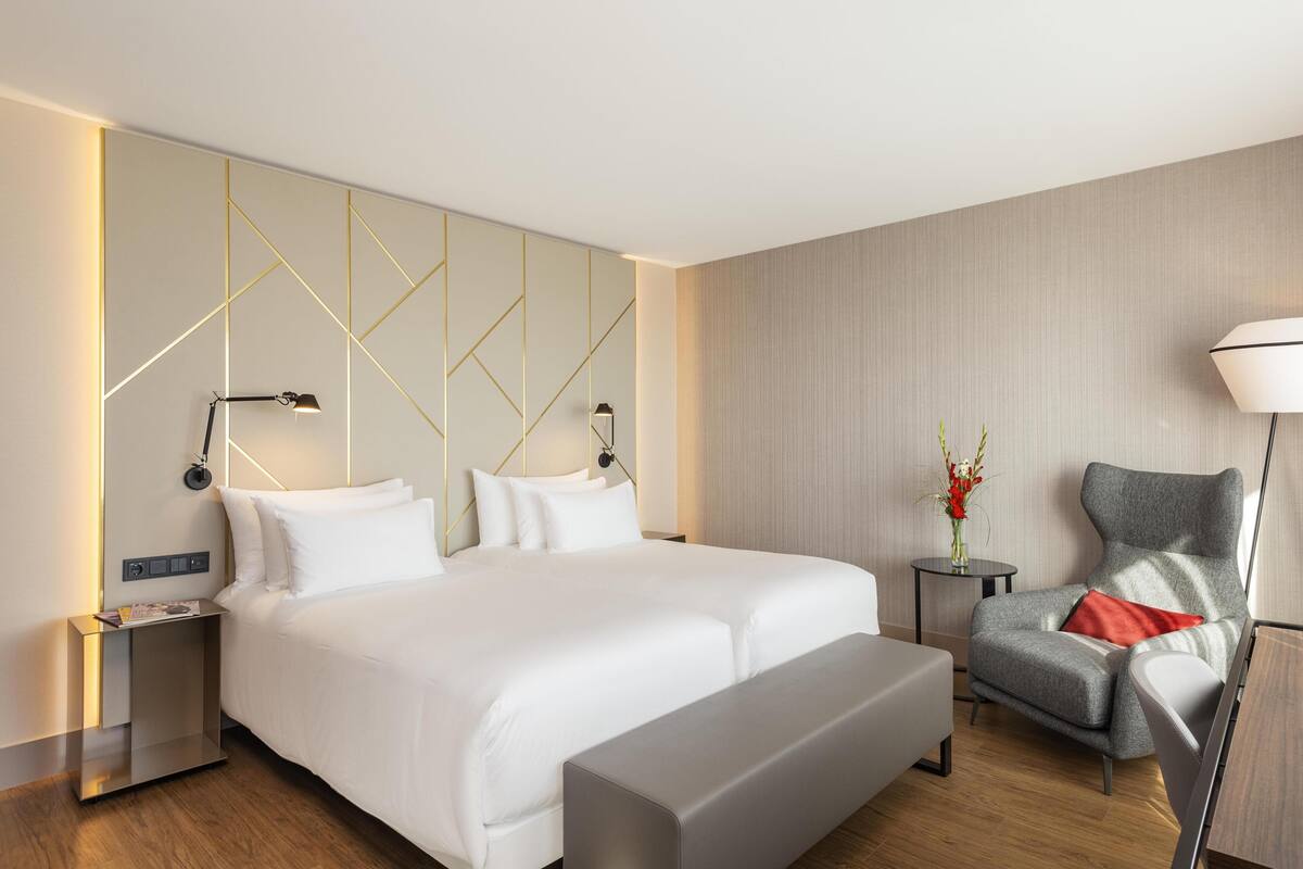 A modern hotel room with a large bed, bedside tables, a chair, and a lamp.