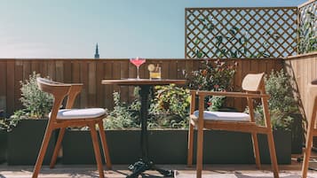 Una terraza de madera con dos sillas y una mesa, rodeada de plantas y una valla de madera.