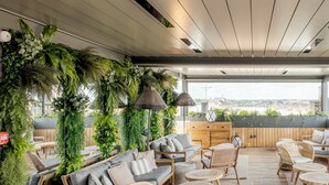 A rooftop lounge with a view, furnished with sofas and chairs, and surrounded by lush greenery.