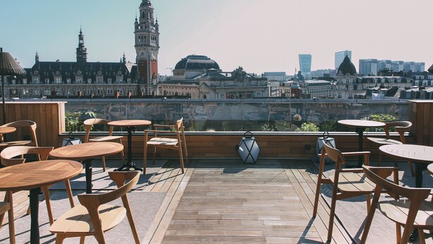A rooftop terrace with wooden tables and chairs, offering a view of historic buildings and modern skyscrapers.