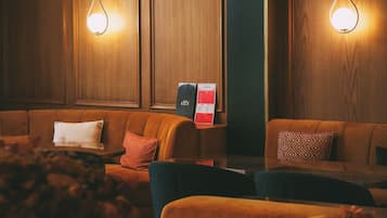 A cozy lounge area with wooden paneling, two wall-mounted light fixtures, and a menu board.