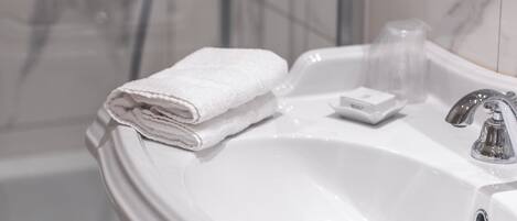 Un baño con lavamanos blanco, una toalla blanca doblada, un jabonera y una zona de ducha.