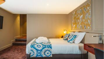 A hotel room with a bed, a desk, a chair, a lamp, and a painting on the wall.