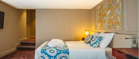 A hotel room with a bed, a desk, a chair, a lamp, and a painting on the wall.