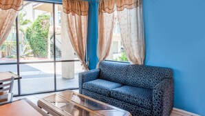 A room with a blue sofa, a wooden coffee table, and a view of the outdoors through large windows with curtains. - Howard Johnson by Wyndham Norco (Norco)